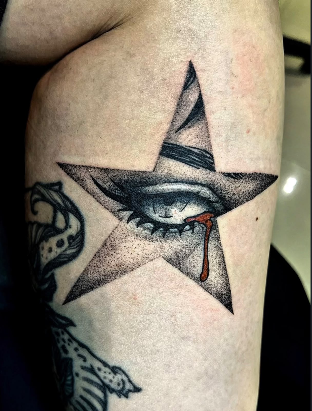 Estrela com olho chorando sangue em dotwork no braço